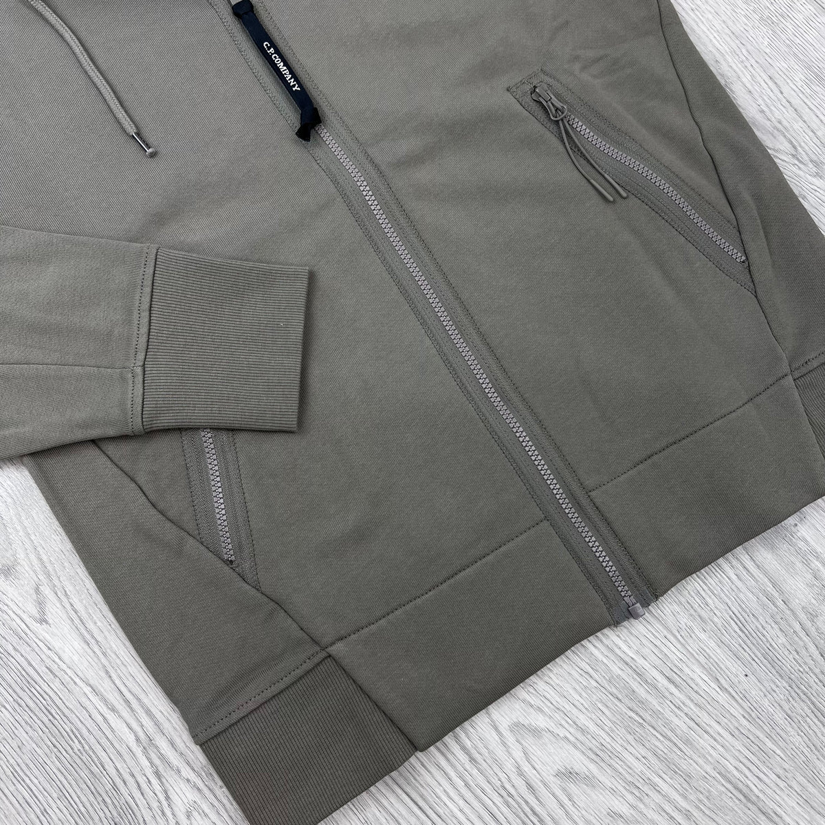 A close up view of the zip and hem on a CP Company Raised Fleece Zip Hoodie in Fallen Rock.