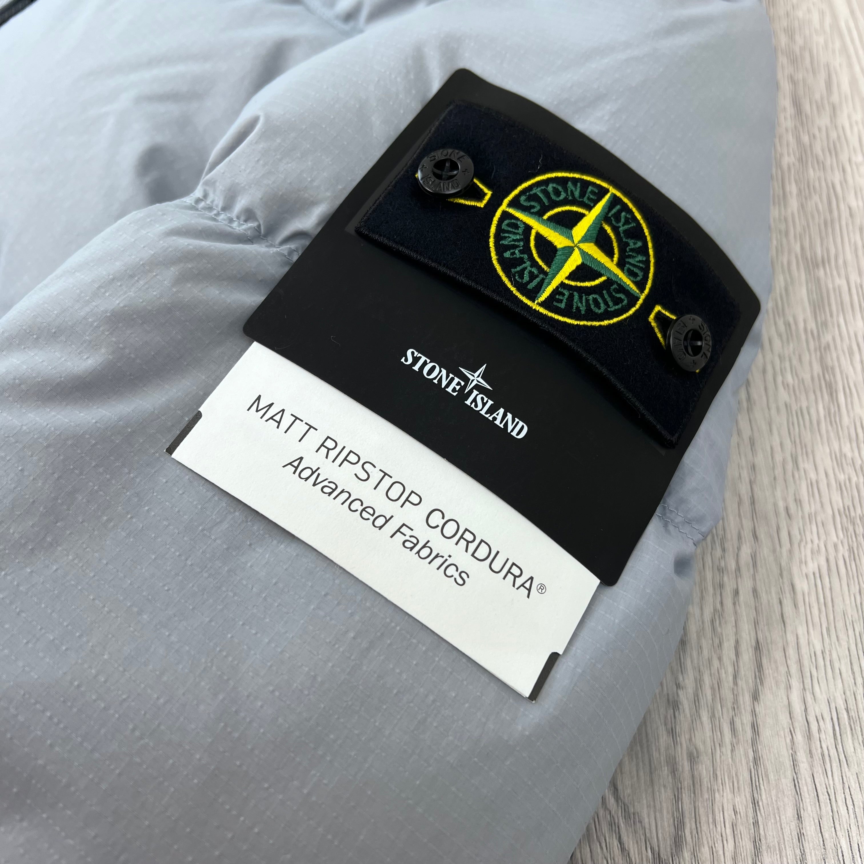 A close up view of the sleeve badge on a Stone Island Matt Ripstop CORDURA® Down Jacket in Ash Grey.